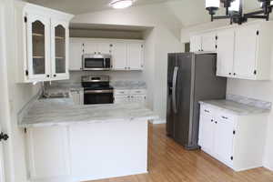 Kitchen with white cabinetry, sink, stainless steel appliances, and vaulted ceiling