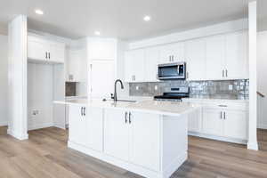 Kitchen featuring appliances with stainless steel finishes, sink, white cabinetry, and a center island with sink