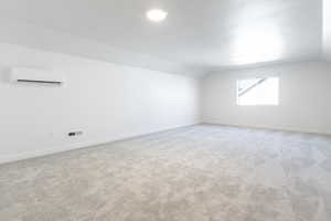 Carpeted empty room with a wall mounted AC and vaulted ceiling