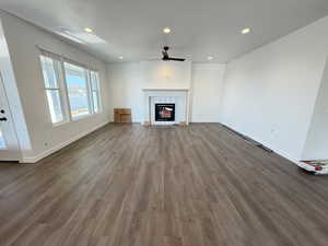 Unfurnished living room featuring ceiling fan, a fireplace, and dark wood-type flooring