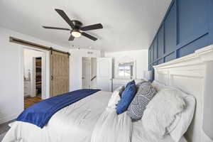 Bedroom with ceiling fan, a barn door, a spacious closet, a textured ceiling, and a walk-in closet