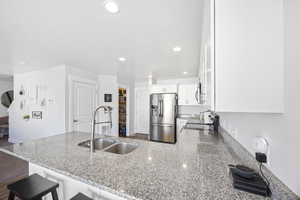 Kitchen with stainless steel refrigerator with ice dispenser, a breakfast bar, sink, white cabinets, and range with electric stovetop