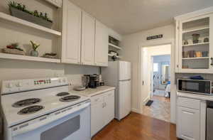 Kitchen featuring a textured ceiling, white appliances, dark hardwood / wood-style floors, and white cabinetry