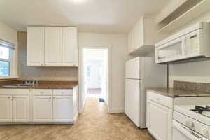 Kitchen with white cabinetry, sink, light carpet, and white appliances