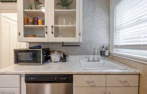 Kitchen featuring light stone counters, sink, white cabinets, and stainless steel dishwasher