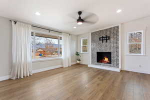 Living room with ceiling fan, light wood-type flooring, a fireplace, and a wealth of natural light