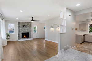 Living room with a fireplace, light hardwood / wood-style flooring, and ceiling fan