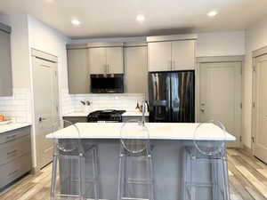 Kitchen with gray cabinetry, a breakfast bar, stainless steel fridge, and an island with sink