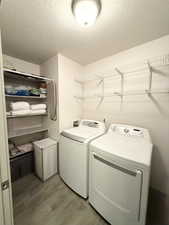 Laundry room with washing machine and clothes dryer, a textured ceiling, and light wood-type flooring