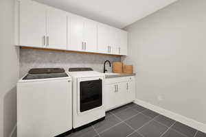 Washroom with cabinets, washer and clothes dryer, dark tile patterned floors, and sink