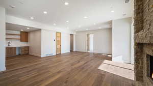 Unfurnished living room featuring built in desk, a stone fireplace, dark wood-type flooring, and sink