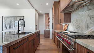 Kitchen with light wood-type flooring, backsplash, premium range hood, sink, and double oven range