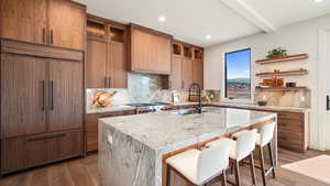 Kitchen featuring a kitchen bar, decorative backsplash, a kitchen island with sink, sink, and paneled built in fridge