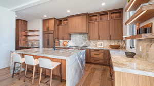 Kitchen featuring backsplash, paneled built in fridge, sink, an island with sink, and wood-type flooring