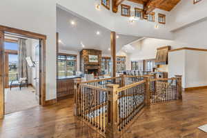 Interior space with beam ceiling, high vaulted ceiling, a stone fireplace, and wood-type flooring