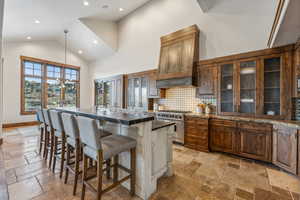 Kitchen with hanging light fixtures, high end stainless steel range, an island with sink, custom range hood, and a breakfast bar area