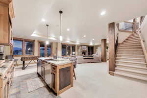 Kitchen with sink, a stone fireplace, light stone counters, an island with sink, and decorative light fixtures