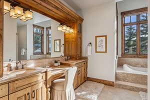 Bathroom with tile patterned flooring, a relaxing tiled tub, and vanity