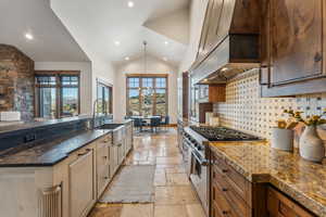 Kitchen with tasteful backsplash, dark stone counters, custom exhaust hood, sink, and range with two ovens