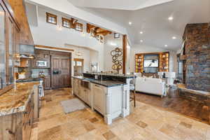 Kitchen featuring sink, built in appliances, a spacious island, dark stone counters, and a kitchen bar