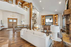 Living room with a fireplace, dark wood-type flooring, high vaulted ceiling, beamed ceiling, and a chandelier