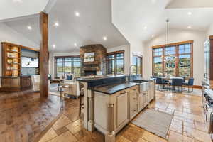 Kitchen with a kitchen island with sink, a kitchen breakfast bar, sink, dark stone countertops, and a fireplace