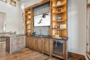 Bar with backsplash, sink, dark stone countertops, hardwood / wood-style floors, and wine cooler