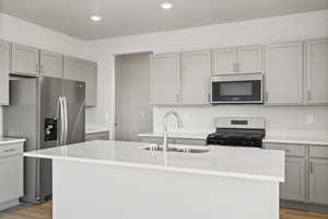 Kitchen featuring appliances with stainless steel finishes, sink, a center island with sink, and light hardwood / wood-style flooring