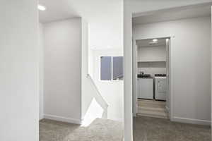 Hallway with light colored carpet and washer and clothes dryer