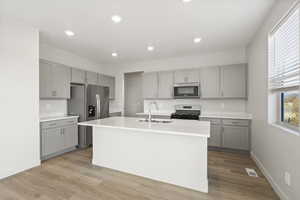 Kitchen featuring stainless steel appliances, sink, a kitchen island with sink, and light hardwood / wood-style flooring