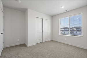 Unfurnished bedroom with light colored carpet, a closet, and a textured ceiling