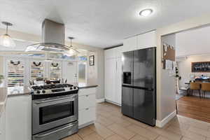 Kitchen with a textured ceiling, decorative light fixtures, island range hood, white cabinetry, and stainless steel appliances