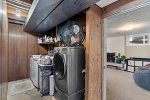 Clothes washing area featuring separate washer and dryer, wooden walls, light colored carpet, and a textured ceiling