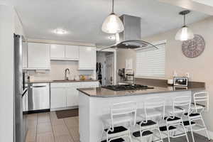 Kitchen featuring white cabinetry, island exhaust hood, kitchen peninsula, decorative light fixtures, and appliances with stainless steel finishes