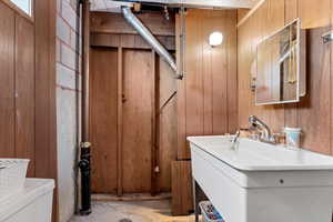 Bathroom with concrete flooring, toilet, wooden walls, and sink