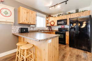 Kitchen with backsplash, kitchen peninsula, light brown cabinetry, black appliances, and light wood-type flooring