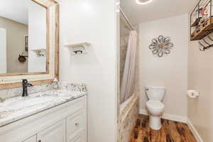 Bathroom with wood finished floors, shower / bath combination with curtain, toilet, vanity, and baseboards