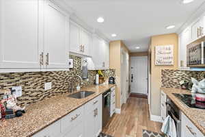 Kitchen with appliances with stainless steel finishes, light stone counters, sink, light hardwood / wood-style flooring, and white cabinetry