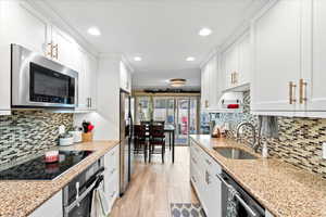 Kitchen with white cabinets, stainless steel appliances, light stone counters, and sink