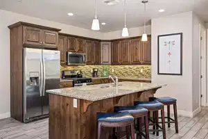 Kitchen featuring decorative backsplash, appliances with stainless steel finishes, a center island with sink, and light stone counters