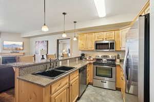 Kitchen with hanging light fixtures, sink, appliances with stainless steel finishes, kitchen peninsula, and a breakfast bar area