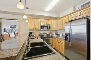 Kitchen featuring pendant lighting, light brown cabinets, sink, and appliances with stainless steel finishes