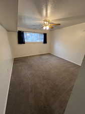 Unfurnished room with ceiling fan, dark carpet, and a textured ceiling