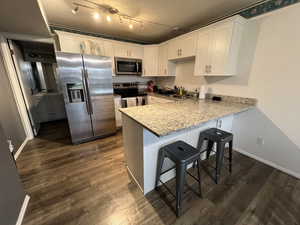 Kitchen with kitchen peninsula, appliances with stainless steel finishes, a textured ceiling, sink, and white cabinets