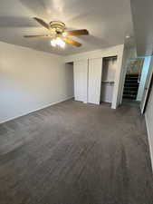 Unfurnished bedroom with dark colored carpet, a textured ceiling, two closets, and ceiling fan