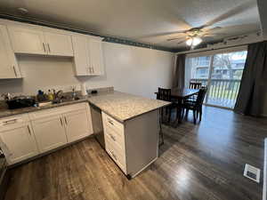 Kitchen featuring ceiling fan, stainless steel dishwasher, kitchen peninsula, a textured ceiling, and white cabinets