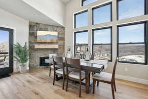 Dining space featuring a stone fireplace, light wood-type flooring, and a high ceiling