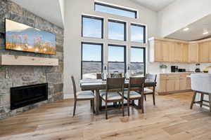 Dining space with a stone fireplace, a high ceiling, and light wood-type flooring