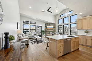 Kitchen with light brown cabinets, stainless steel dishwasher, light hardwood / wood-style floors, decorative light fixtures, and a kitchen island with sink