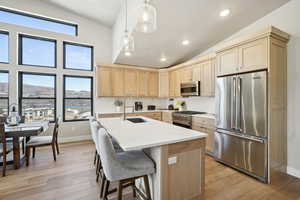 Kitchen featuring sink, hanging light fixtures, vaulted ceiling, light brown cabinetry, and stainless steel appliances